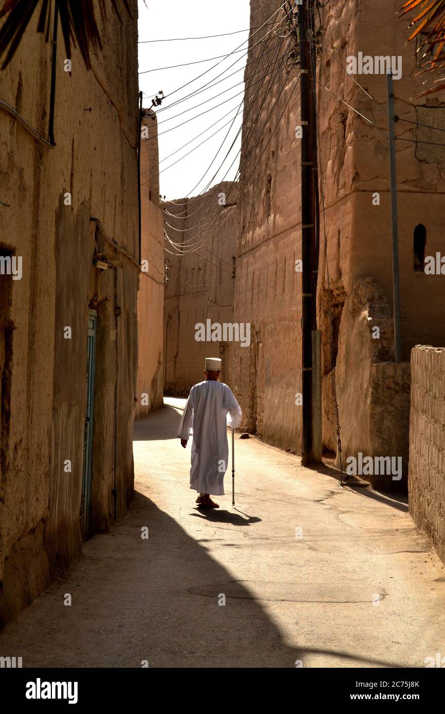 Alter Mann in einem traditionellen omanischen Kleid zu Fuß auf der schmalen Straße in Nizwa, Oman Stockfoto
