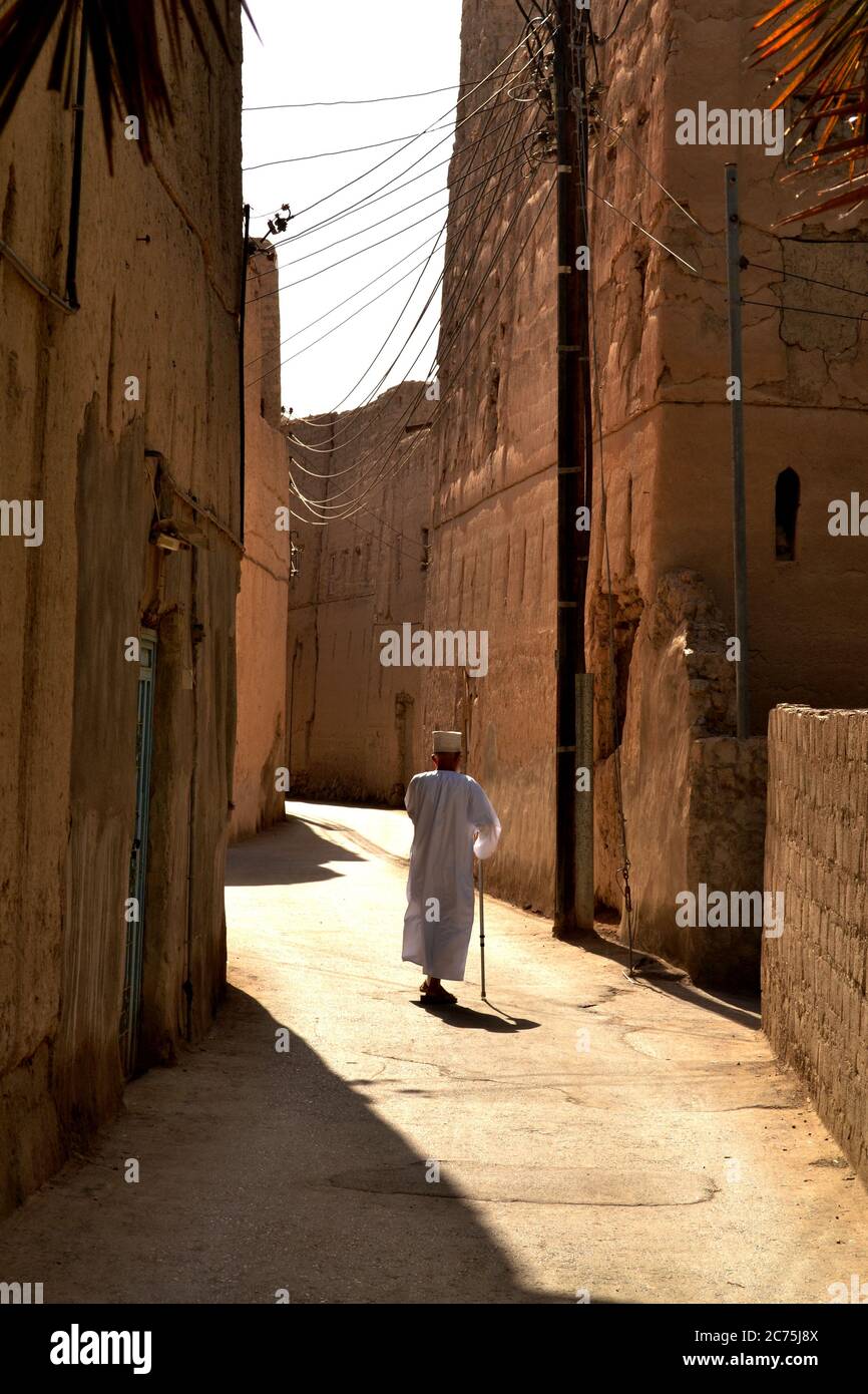 Alter Mann in einem traditionellen omanischen Kleid zu Fuß auf der schmalen Straße in Nizwa, Oman Stockfoto