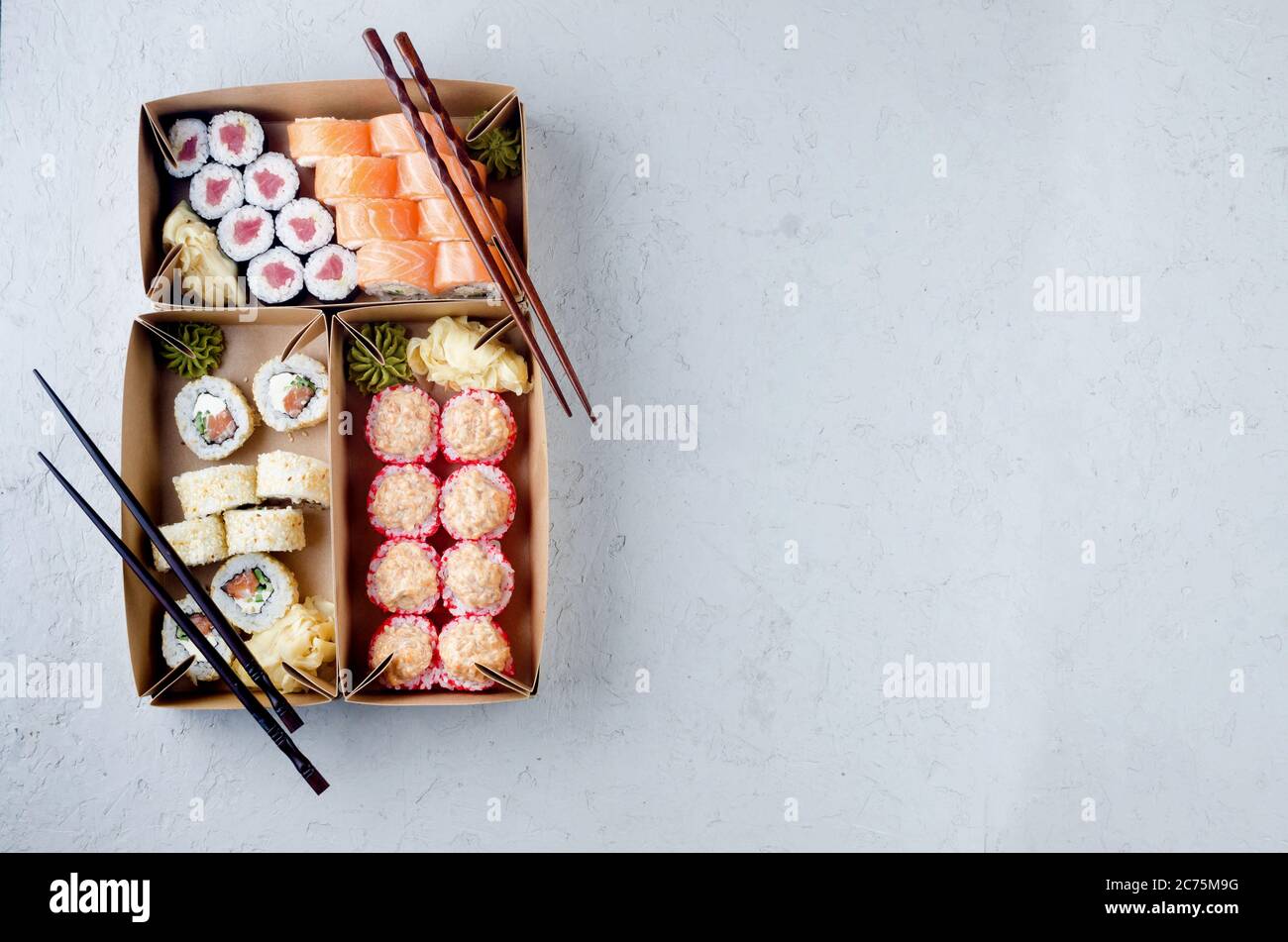 Leckere Sushi-Brötchen in Einweg-Kraftpapier-Boxen, Saucen, Essstäbchen. Sushi zum Mitnehmen oder Anliefern Stockfoto