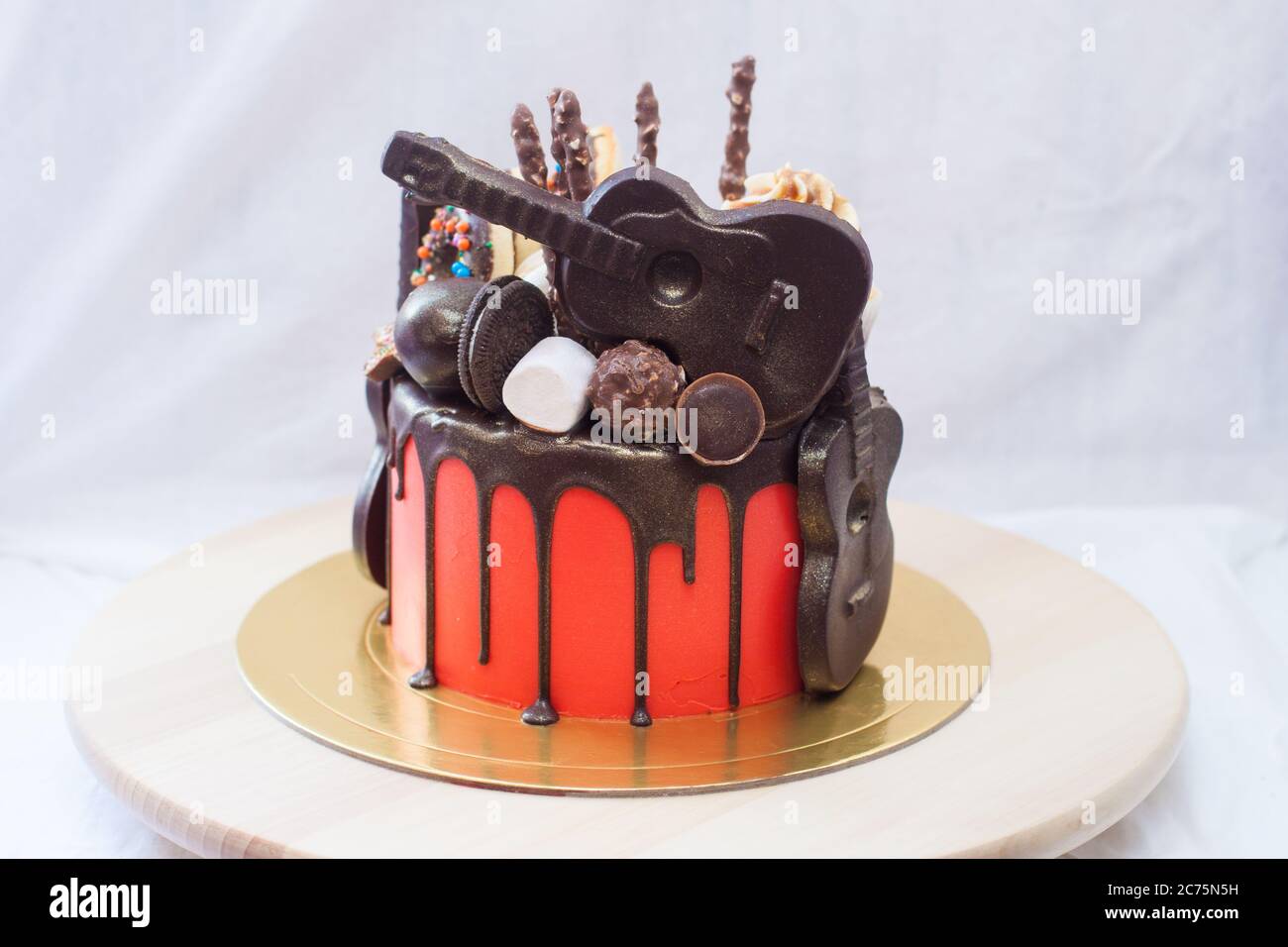 Roter Kuchen mit geschmolzener Schokolade, Marshmallow, Bonbons, Toffees, Gitarren, Donuts, Cake Pops und Sternen Dekoration. Stockfoto Roter Kuchen mit geschmolzener Schokolade, Marshmallow, Bonbons, Toffees, Gitarren, Donuts, Cake Pops und Sternen Dekoration. Stockfoto