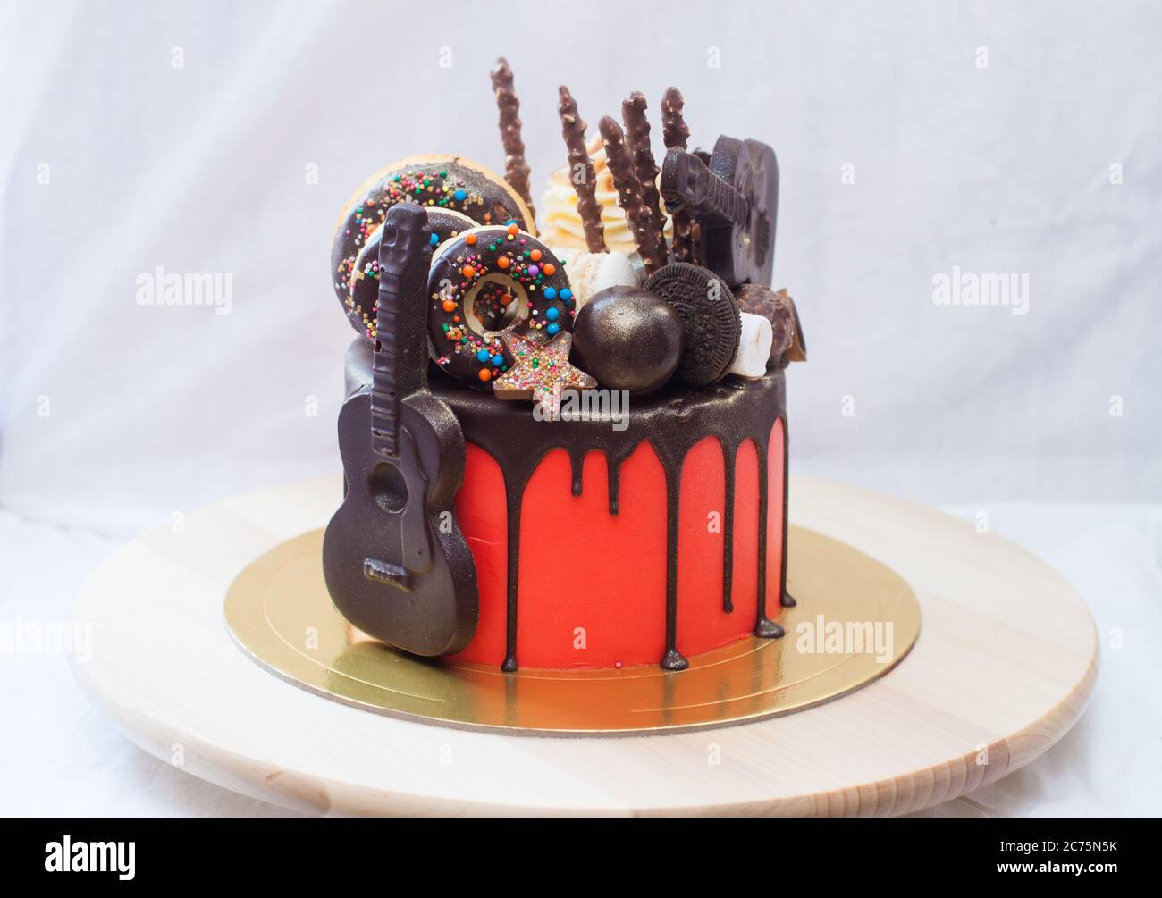 Roter Kuchen mit geschmolzener Schokolade, Marshmallow, Bonbons, Toffees, Gitarren, Donuts, Cake Pops und Sternen Dekoration. Stockfoto Roter Kuchen mit geschmolzener Schokolade, Marshmallow, Bonbons, Toffees, Gitarren, Donuts, Cake Pops und Sternen Dekoration. Stockfoto