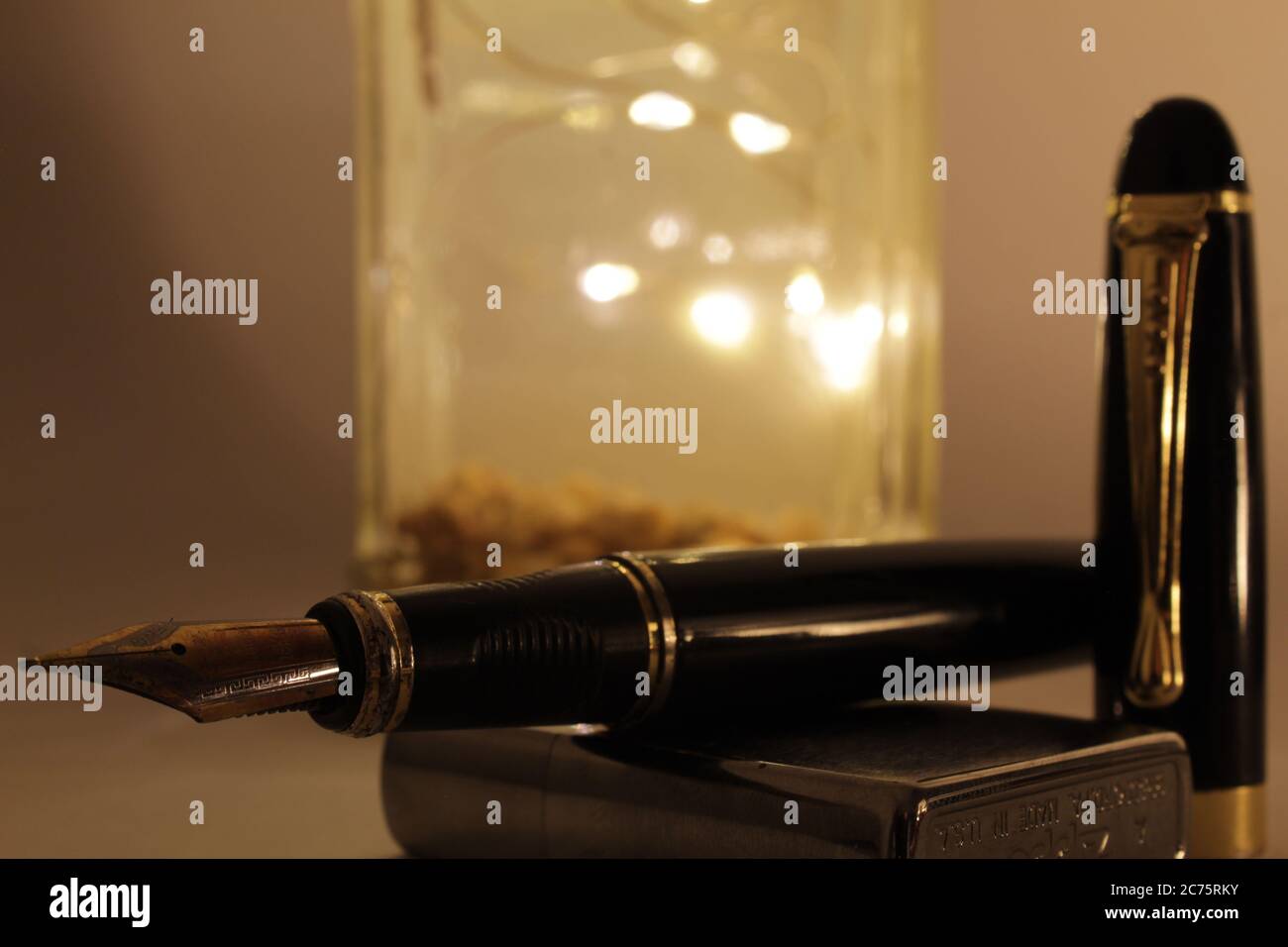 Füllfederhalter über einem zippo Feuerzeug mit einer handgefertigten Lampe als Hintergrund Stockfoto