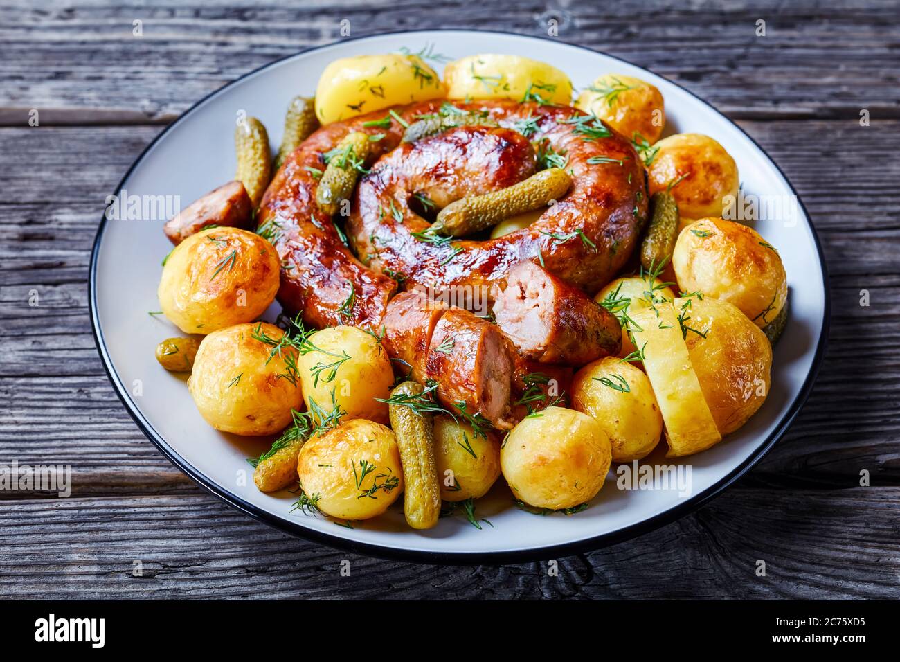 Altmodisches deutsches Gericht: Junge Kartoffeln gekocht und gebraten, serviert mit Schweinewurst und eingelegten Gurken, bestreut mit frischem Dill, serviert auf einem Teller Stockfoto