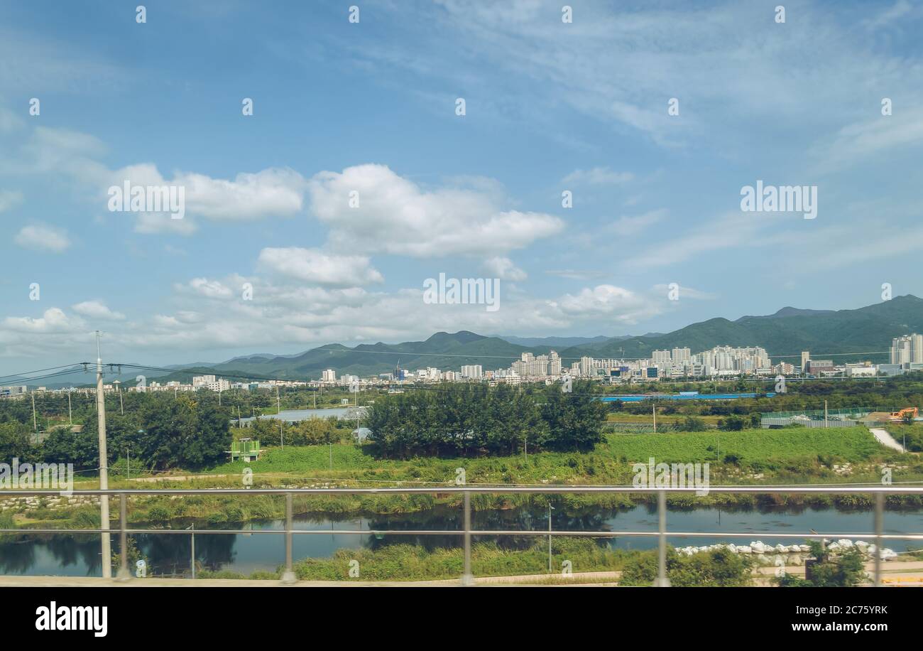 Blick von oben auf den kleinen Kanal und ein kleines koreanisches Stadtbild weit entfernt mit flauschigen Wolken am Himmel Stockfoto