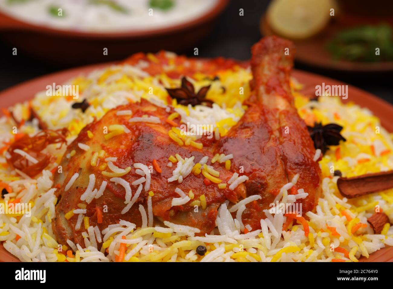 Huhn Biryani , Tandoori Huhn mit Basmathi Reis und Raita als Beilage in einem Steingut und einer Tasse heißen Minztee mit schwarzem Backgro angeordnet Stockfoto