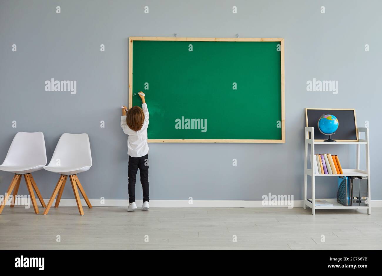 Rückansicht des kleinen Jungen, der während des Unterrichts etwas auf einer Tafel schreibt oder zeichnet. Kind, das in der Schule studiert Stockfoto