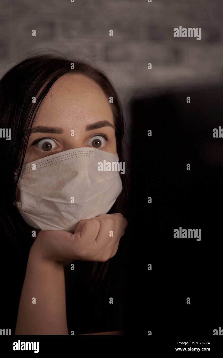 Eine Frau in einer medizinischen Maske erfährt mit einem Laptop aus dem Internet Neuigkeiten über das Coronavirus. Frau ist besorgt über seine Gesundheit. Die Epidemie Von Stockfoto