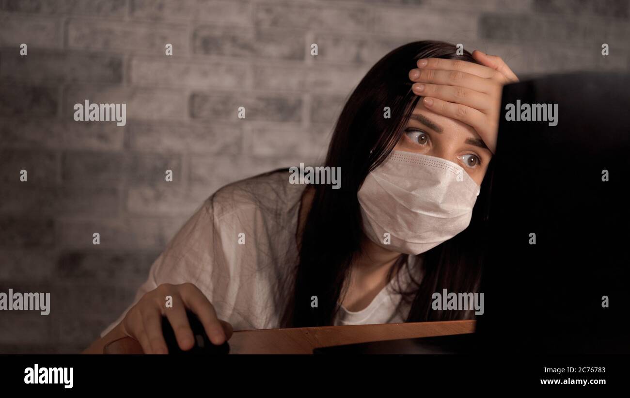 Eine Frau in einer medizinischen Maske erfährt mit einem Laptop aus dem Internet Neuigkeiten über das Coronavirus. Frau ist besorgt über seine Gesundheit. Die Epidemie Von Stockfoto