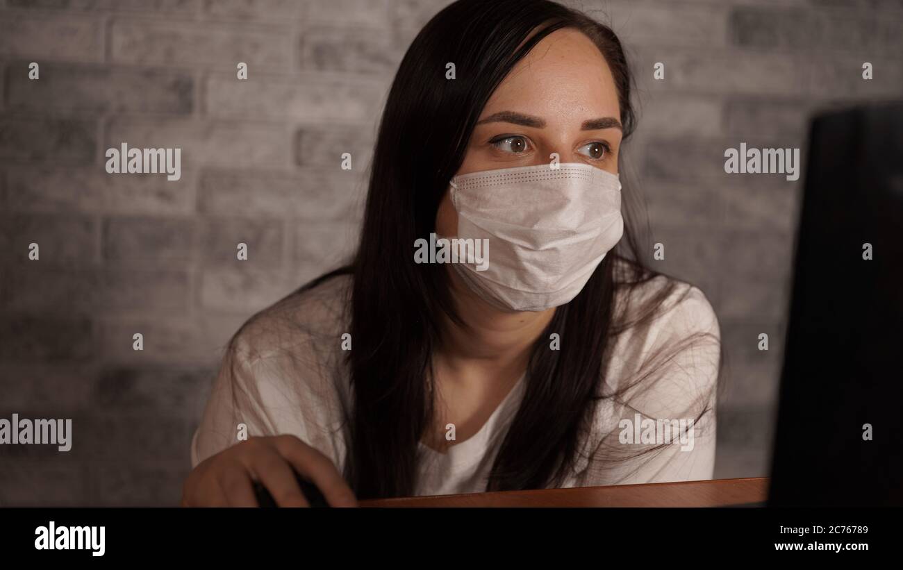 Eine Frau in einer medizinischen Maske erfährt mit einem Laptop aus dem Internet Neuigkeiten über das Coronavirus. Frau ist besorgt über seine Gesundheit. Die Epidemie Von Stockfoto
