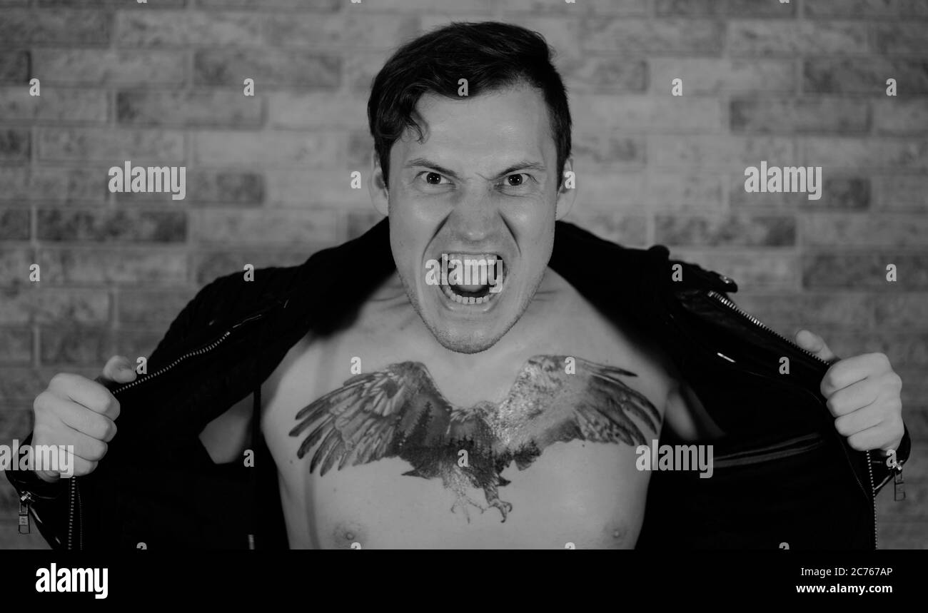 Ein Mann in einer modischen Jacke auf grauem Hintergrund. Porträt eines wütenden jungen Mannes in einer Lederjacke runzelt die Stirn vor der Kamera Stockfoto