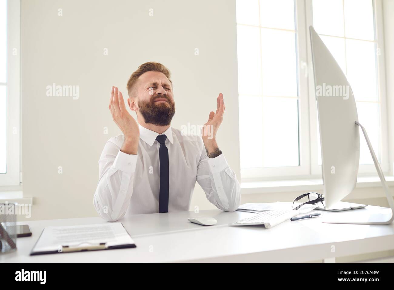 Der verärgerte, müde Geschäftsmann hob seine Hände auf und sah einen Computer an einem Schreibtisch im Büro an. Stockfoto