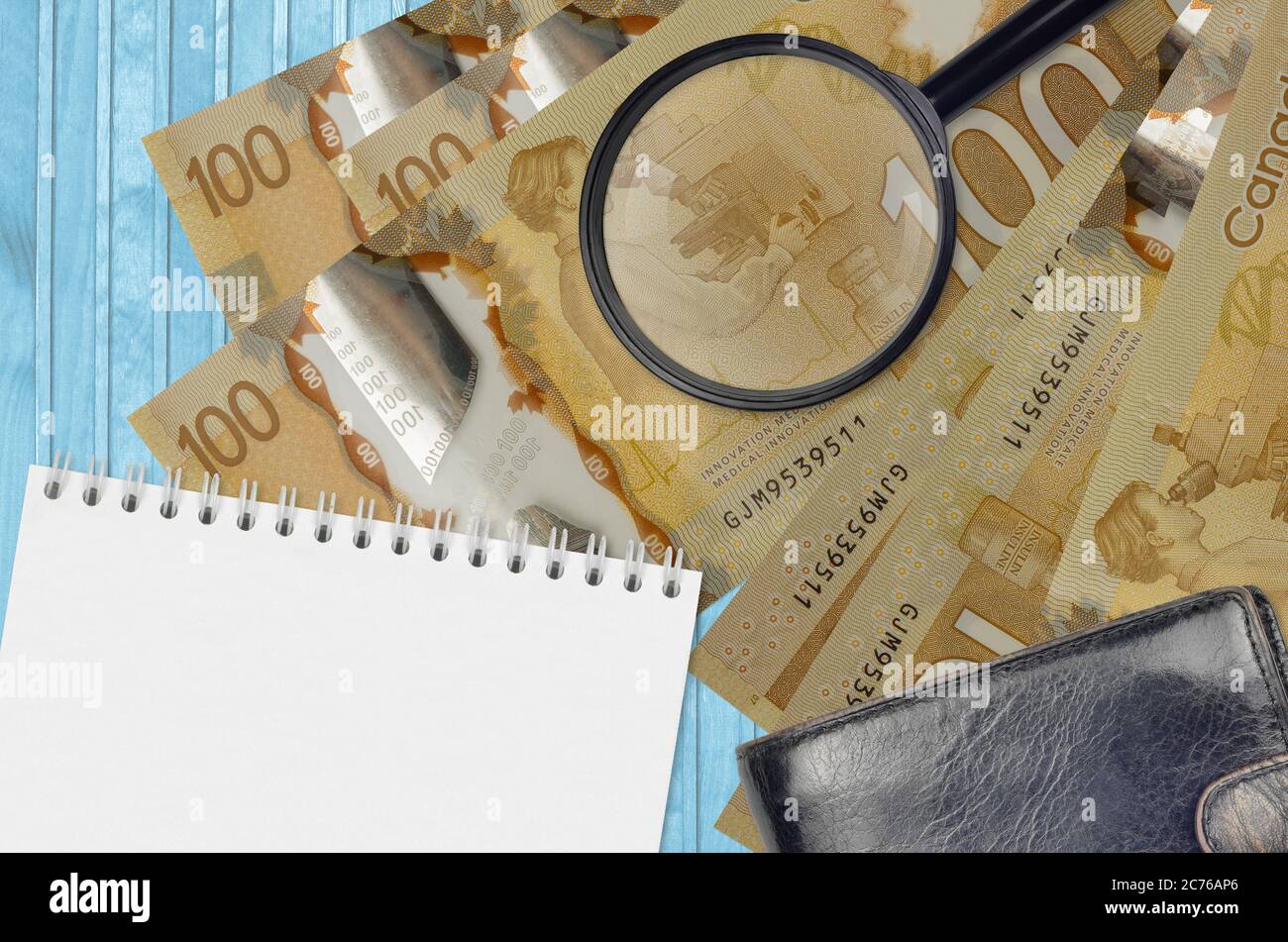 100 kanadische Dollar Scheine und Lupe mit schwarzem Geldbeutel und Notizblock. Konzept von gefälschtem Geld. Suchen Sie nach Unterschieden in Details zu Geld Stockfoto