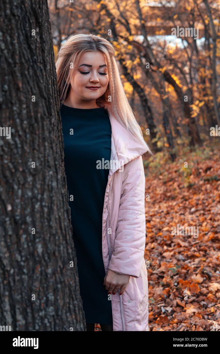 Schöne Frau, die hinter dem Baum herausschaut. Ziemlich ruhige Frau, die Baum berührt und die Kamera in einem ruhigen Wald anschaut Stockfoto
