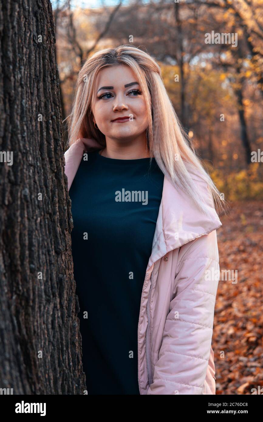 Seriöse Frau, die hinter dem Baum herausschaut. Ziemlich ruhige Frau, die Baum berührt und die Kamera in einem ruhigen Wald anschaut Stockfoto