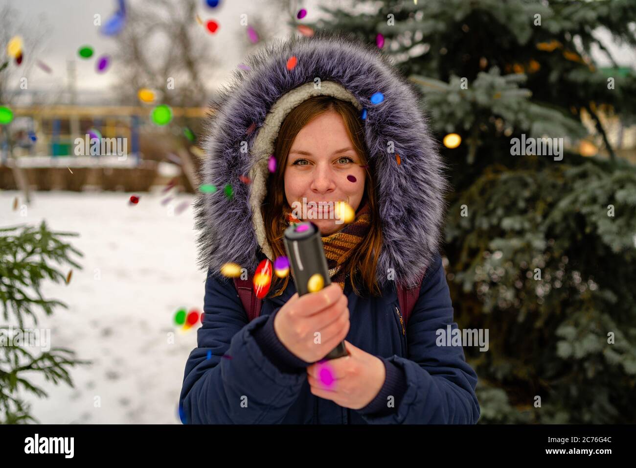 Emotional Frau knallt Konfetti Petard und öffnet ihren Mund vor Freude. Erwachsene Frau in Kapuzenjacke bewundert und knallt Konfetti Petard in die Kamera Stockfoto