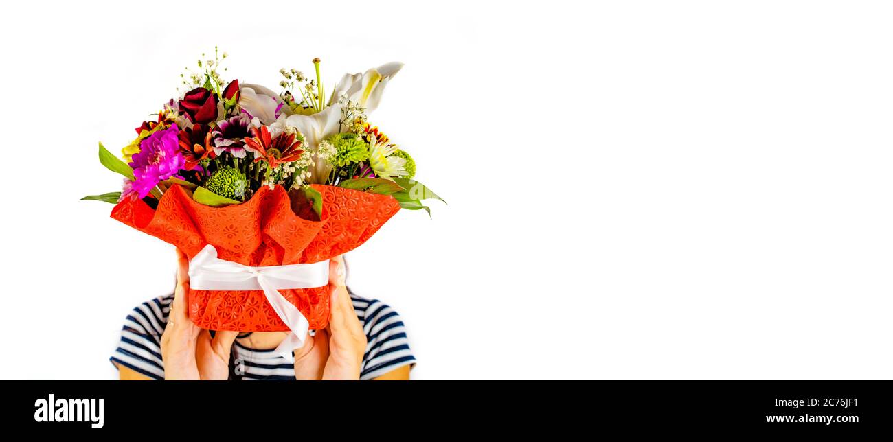 Frau versteckt ihr Gesicht hinter dem Korb von Röschen. Frauen Hände halten bunte Blumenstrauß. Zusammensetzung von verschiedenen Blumen in Wickelkorb auf Stockfoto