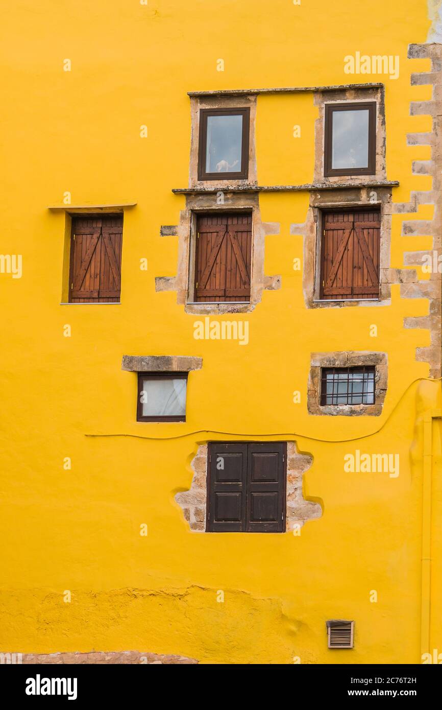 Warme gelbe Fassade mit rustikalen Fenstern in verschiedenen Formen und Größen. Stockfoto