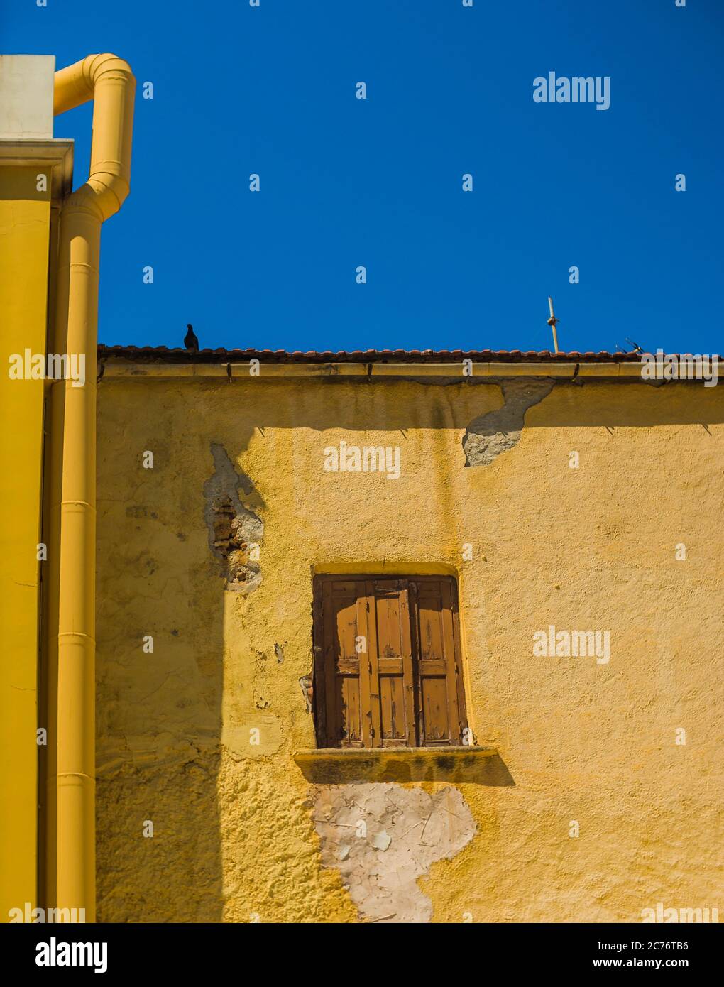 Rustikales braunes Holzfenster an der gelben Fassade eines alten mediterranen Hauses. Blauer Himmel als Hintergrund. Stockfoto