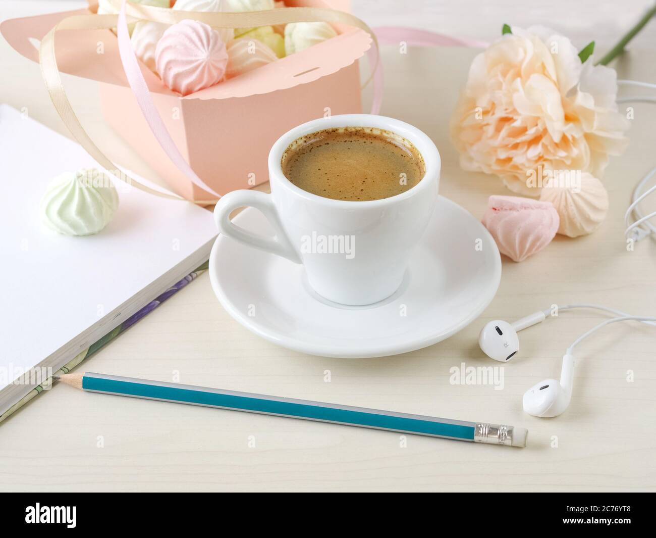 Morgenkaffee mit Notizbuch und Bleistift, mit einer Schachtel gefüllt mit kleinen Baisern, Kopfhörer auf einem hellen Holzhintergrund. Stockfoto