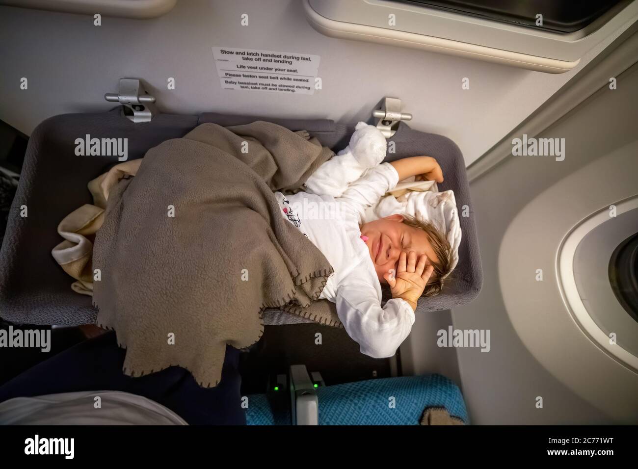 Kleinkind Passagier Kleinkind wacht auf dem Flugzeug und streckt in speziellen Baby-Liegewand Stockfoto