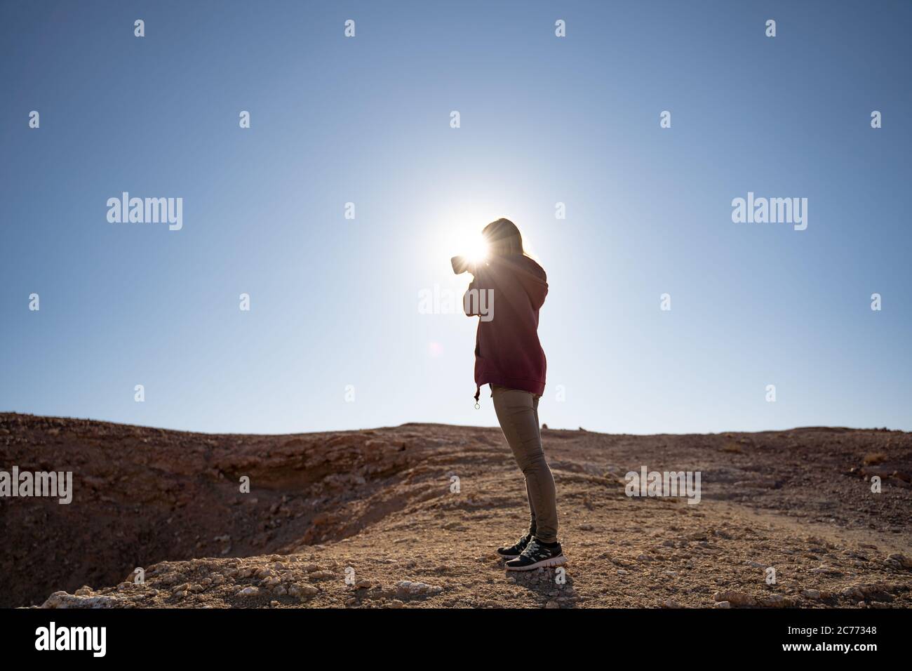 Frau fotografiert, während sie gegen die helle Sonne an Land in der Wüste steht Stockfoto