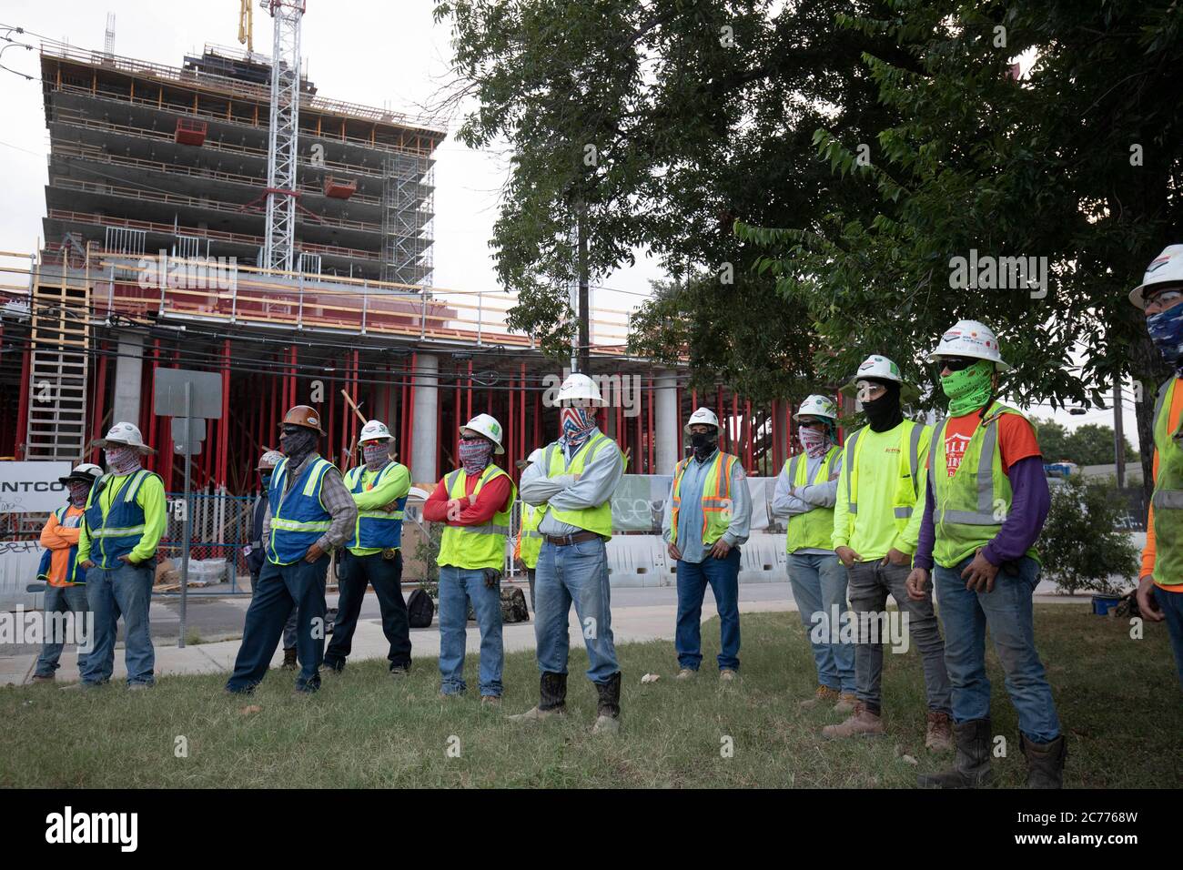 Austin, TX USA 14. Juli 2020: Bauarbeiter hören sich Sicherheitsunterweisungen an, während sie sich auf eine achtstündige Schicht in der 105-Grad-Hitze von Texas vorbereiten. Die Crews befinden sich im zweiten Stock eines geplanten 53-stöckigen Gebäudes, um Vorkehrungen gegen die Coronavirus-Pandemie zu treffen. Stockfoto