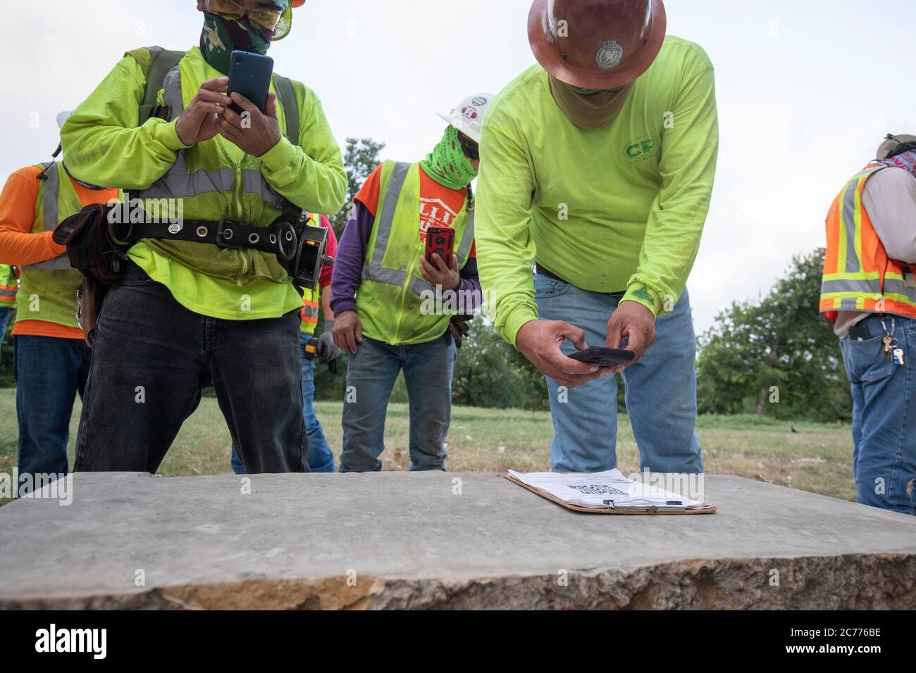 Austin, TX USA 14. Juli 2020: Bauarbeiter scannen mit ihrem Handy einen QR-Code, der ihnen ihren Zeitplan für den Tag gibt, während sie sich auf eine achtstündige Schicht vorbereiten, die ein Hochhaus in der 105-Grad-Hitze von Texas errichtet. Die Crews befinden sich im zweiten Stock eines geplanten 53-stöckigen Gebäudes und treffen gleichzeitig Vorkehrungen gegen die Coronavirus-Pandemie. Stockfoto