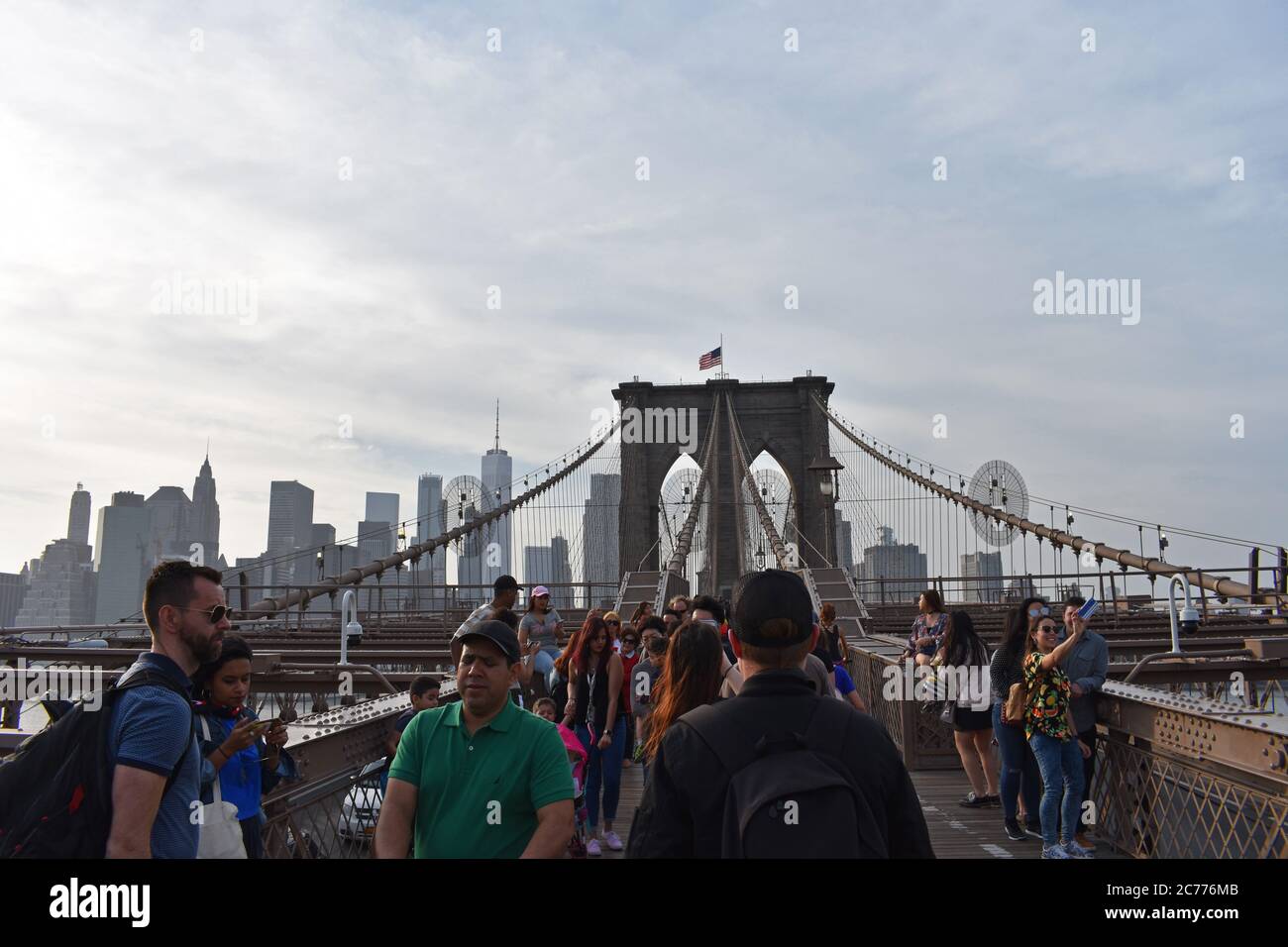 Besucher machen Selfies, bewundern die Aussicht und überqueren die Brooklyn Bridge in New York City. Hinter den Wolkenkratzern der Innenstadt sind die Wolkenkratzer zu sehen. Stockfoto