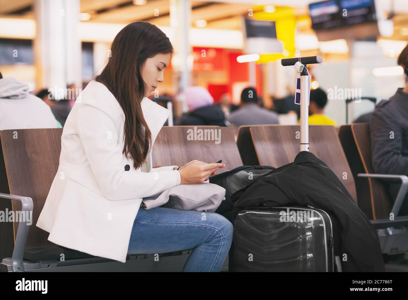 Die Flugpassagin auf dem Handy wartet auf einen verspäteten Flug und sitzt mit Gepäck am Terminal Gate. Gelangweilte und müde Person Stockfoto