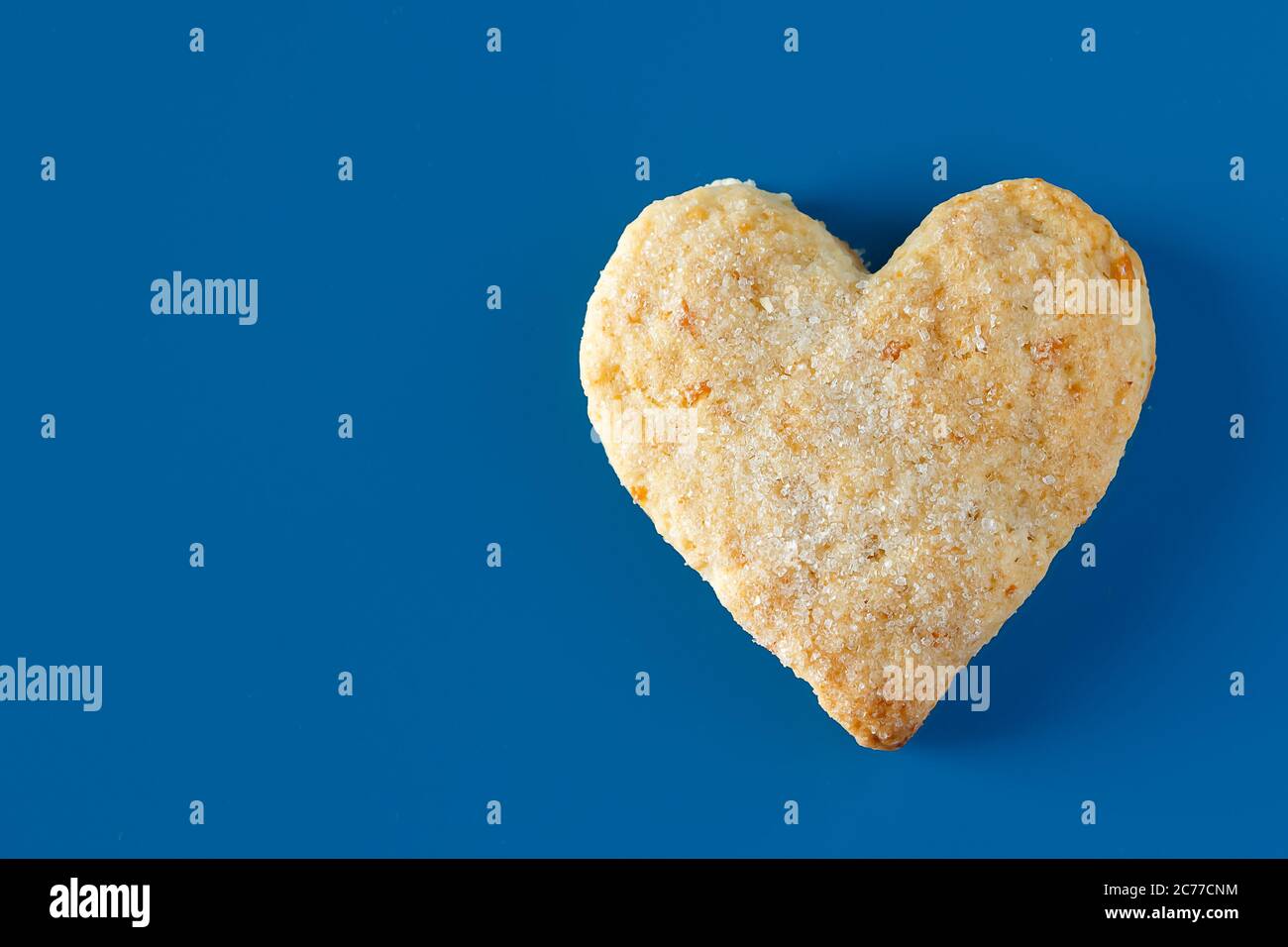 Herzförmige Zuckerkeks auf blauem Hintergrund. Ein süßes herzförmiges Cookie auf blauem Hintergrund, trendige Farbe des Jahres, Platz für Text Stockfoto