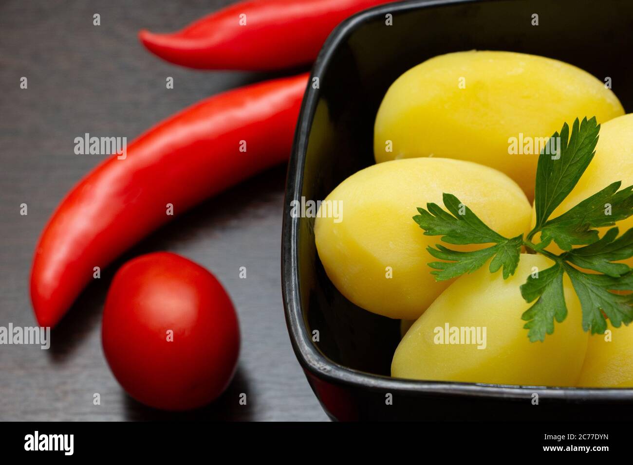 Gekochte Kartoffeln mit Chilischoten und Tomaten auf dunklem Hintergrund Stockfoto