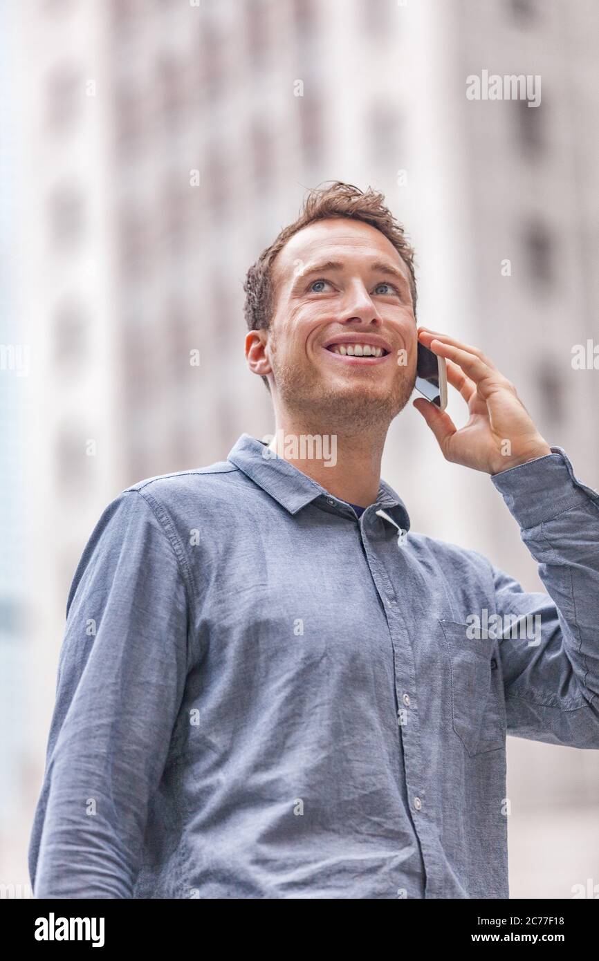 Junger städtischer Geschäftsmann, der in der Stadt auf der Straße telefoniert und am Handy spricht. Glücklich lächelnden Mann Porträt draußen mit Gebäude Stadtbild Hintergrund Stockfoto