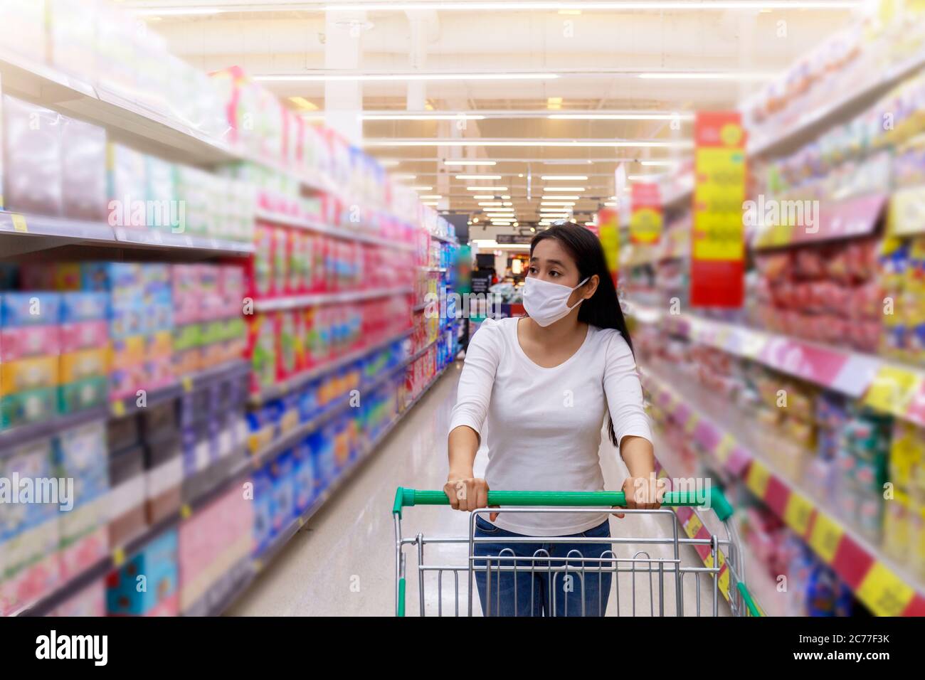 Asiatische Frau tragen Gesichtsmaske Push Warenkorb im Supermarkt. Mädchen suchen Lebensmittel, etwas während Coronavirus Krise oder covid19 Ausbruch zu kaufen. Wom Stockfoto