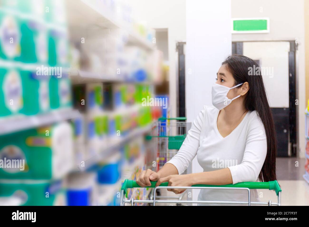 Asiatische Frau tragen Gesichtsmaske Push Warenkorb im Supermarkt. Mädchen suchen Lebensmittel, etwas während Coronavirus Krise oder covid19 Ausbruch zu kaufen. Wom Stockfoto