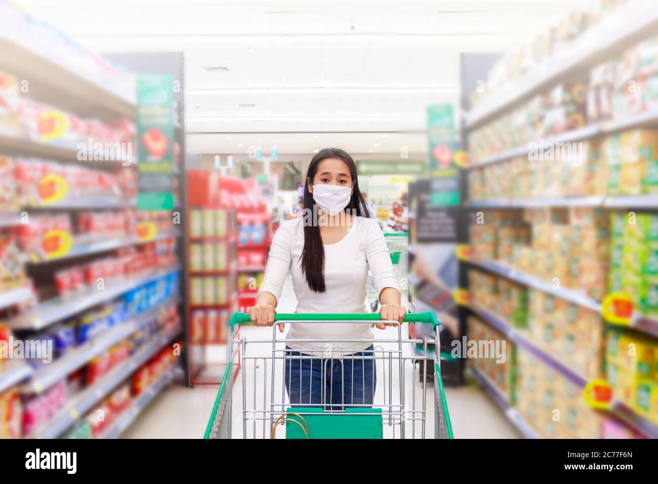 Asiatische Frau tragen Gesichtsmaske Push Warenkorb im Supermarkt Kaufhaus. Mädchen suchen Lebensmittel, etwas zu kaufen. Während der Coronavirus-Krise oder CO Stockfoto