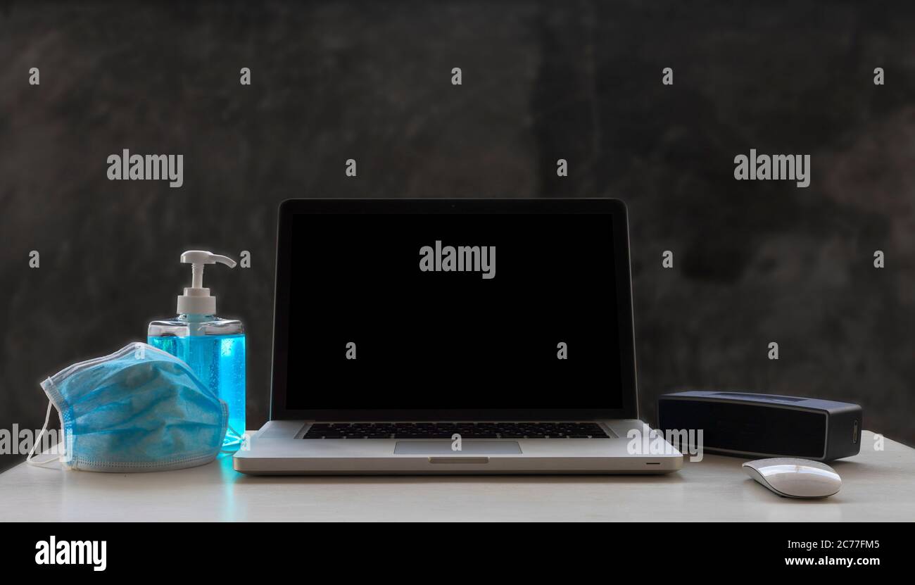 Laptop, Maus, Lautsprecher, Alkohole Gel und medizinische Maske auf weißem Holztisch und rohem Zementhintergrund mit Copyspace für Text oder Design. Stockfoto