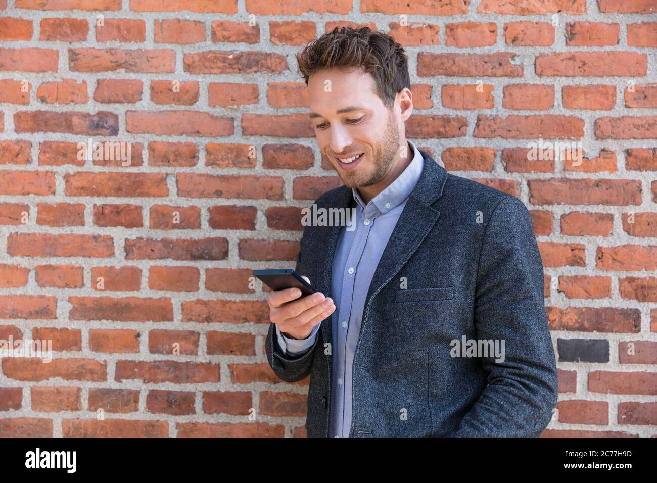 Junge Geschäftsmann mit Smartphone in der Stadt Hintergrund entspannend auf Backsteinmauer SMS auf Handy-App leben einen modernen Lebensstil. Glücklich Stockfoto