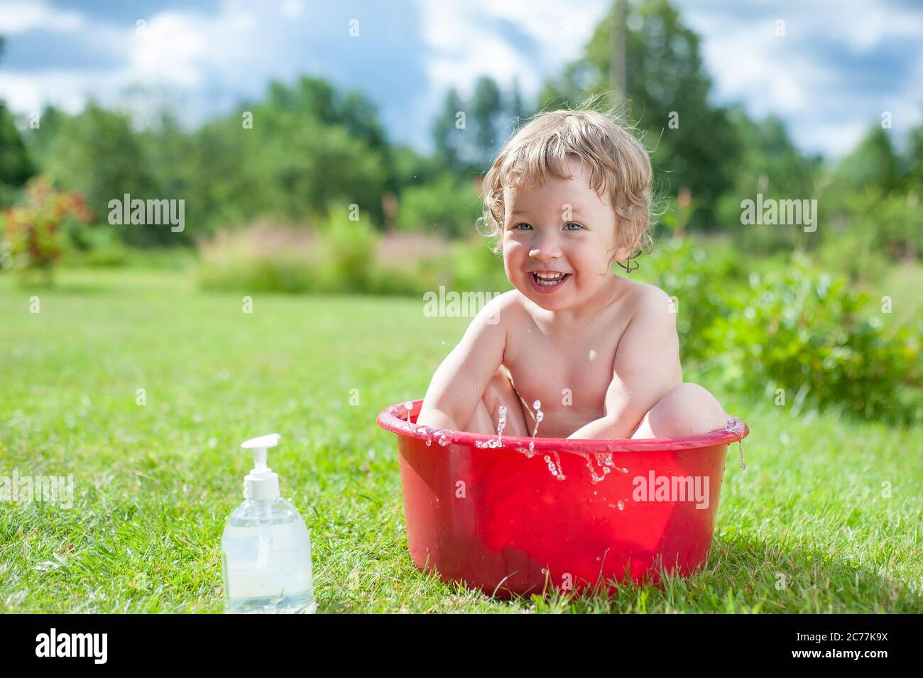 Kleines Baby wäscht im Bad auf dem grünen Gras. Kleines Baby, das Spaß hat,  spritzt Wasser und lacht. Glückliches Kind, das draußen auf grünem Gras  baden kann Stockfotografie - Alamy