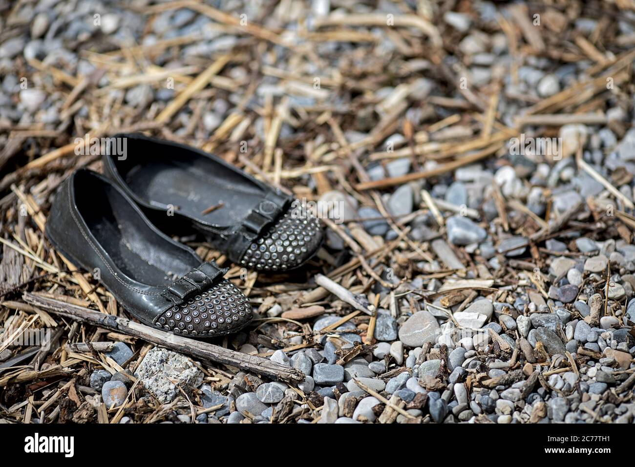 Schwarze schmutzige Kinderschuhe zwischen Kieselsteinen und Stroh Stockfoto