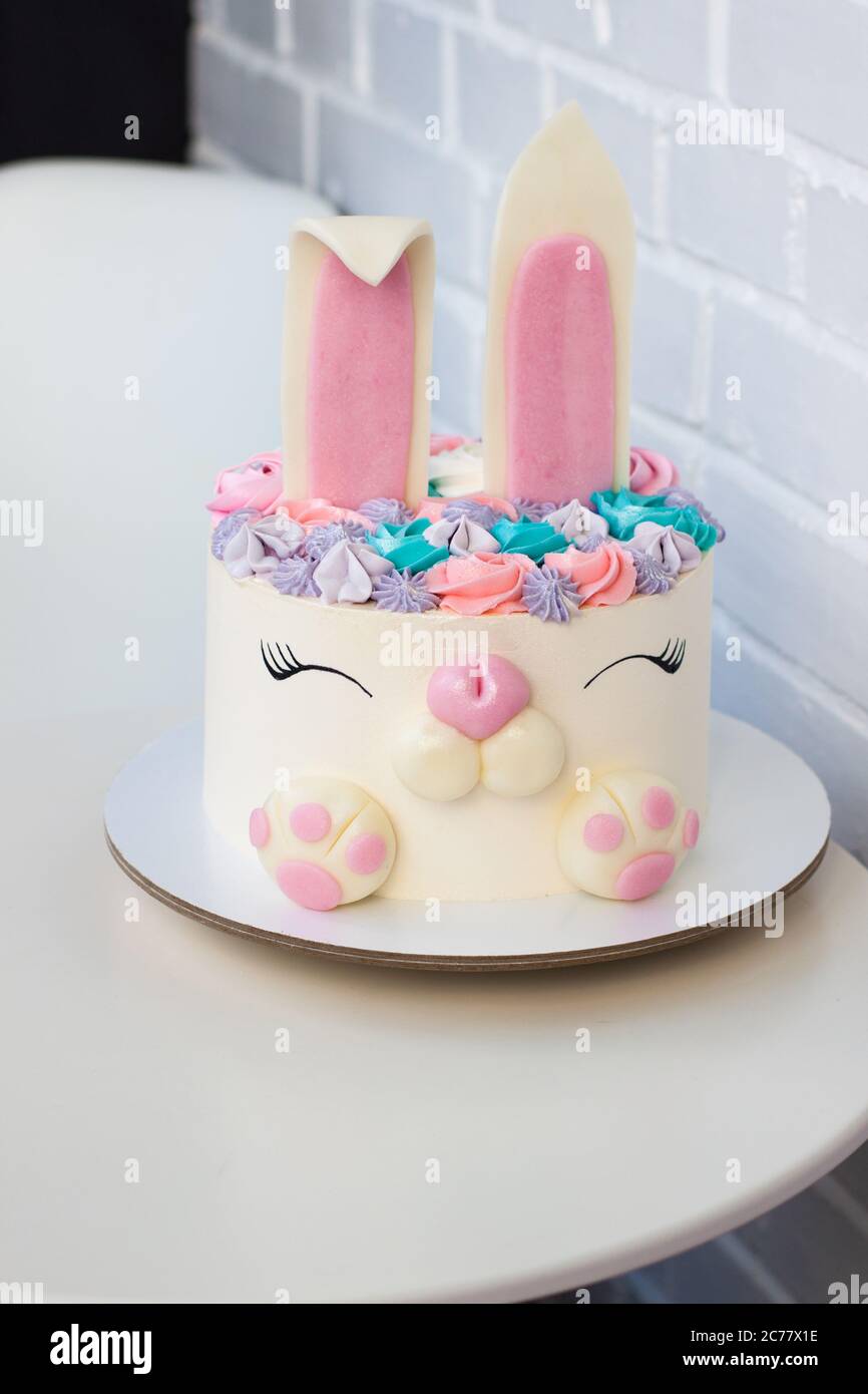 Weiß-rosa Kuchen mit niedlichen Hase zum Kindergeburtstag. Hase aus Fondant und Buttercreme. Weißer Hintergrund. Stockfoto