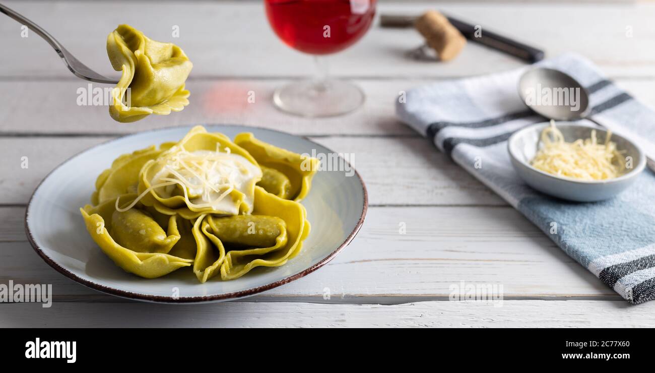 Hausgemachte Bio-Tortellini mit Spinat und Käse auf einem weißen Tisch mit einem Glas Wein auf der Seite. Stockfoto