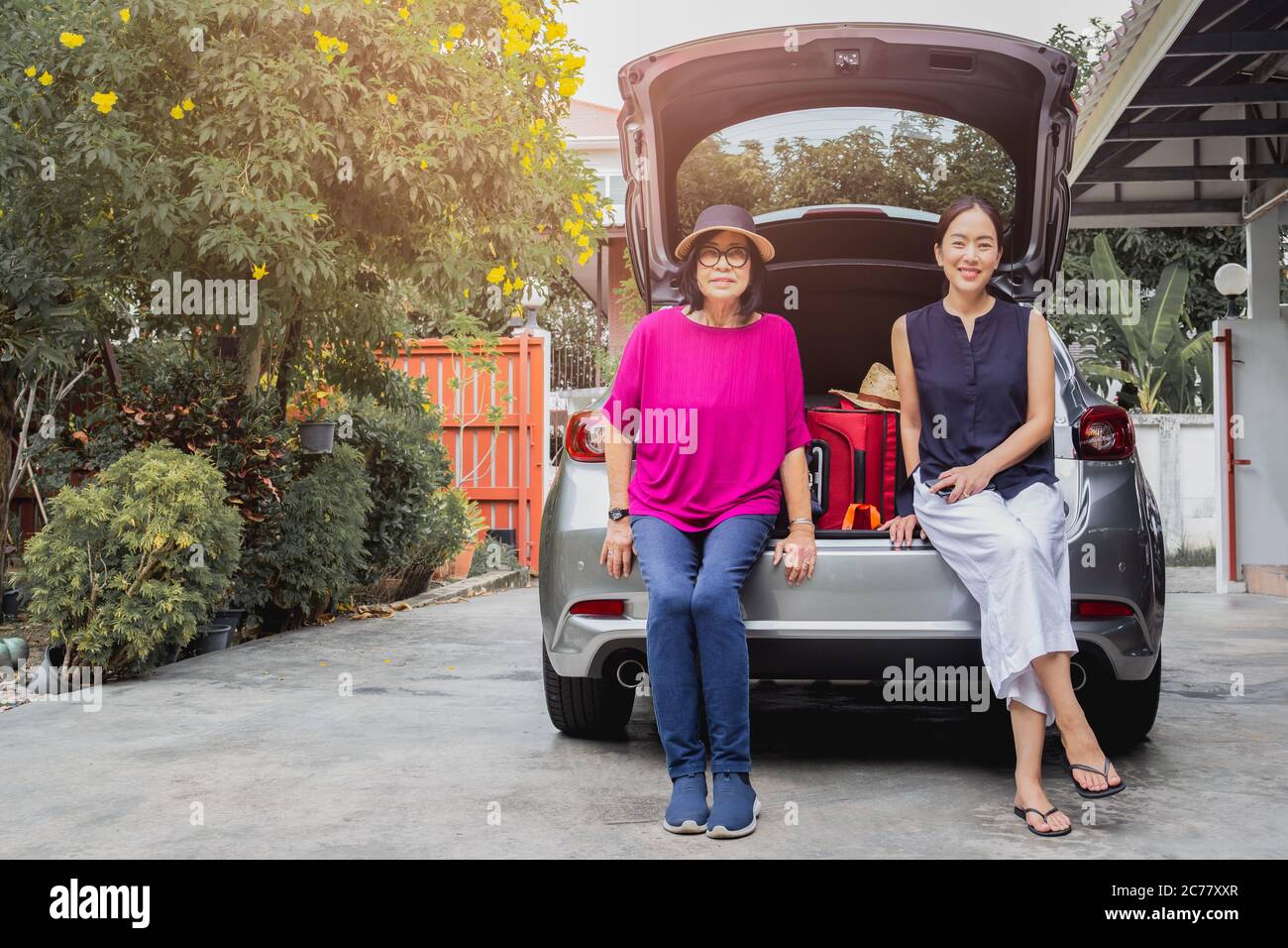 Zwei Frauen sitzen hinter dem Auto, mit Koffern auf Autotour. Stockfoto