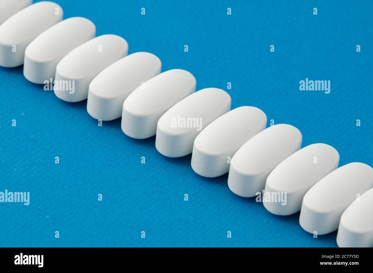 Reihe von weißen Vitamin-Tabletten Drogen liegen auf lebendige blaue Farbe Oberfläche Stockfoto