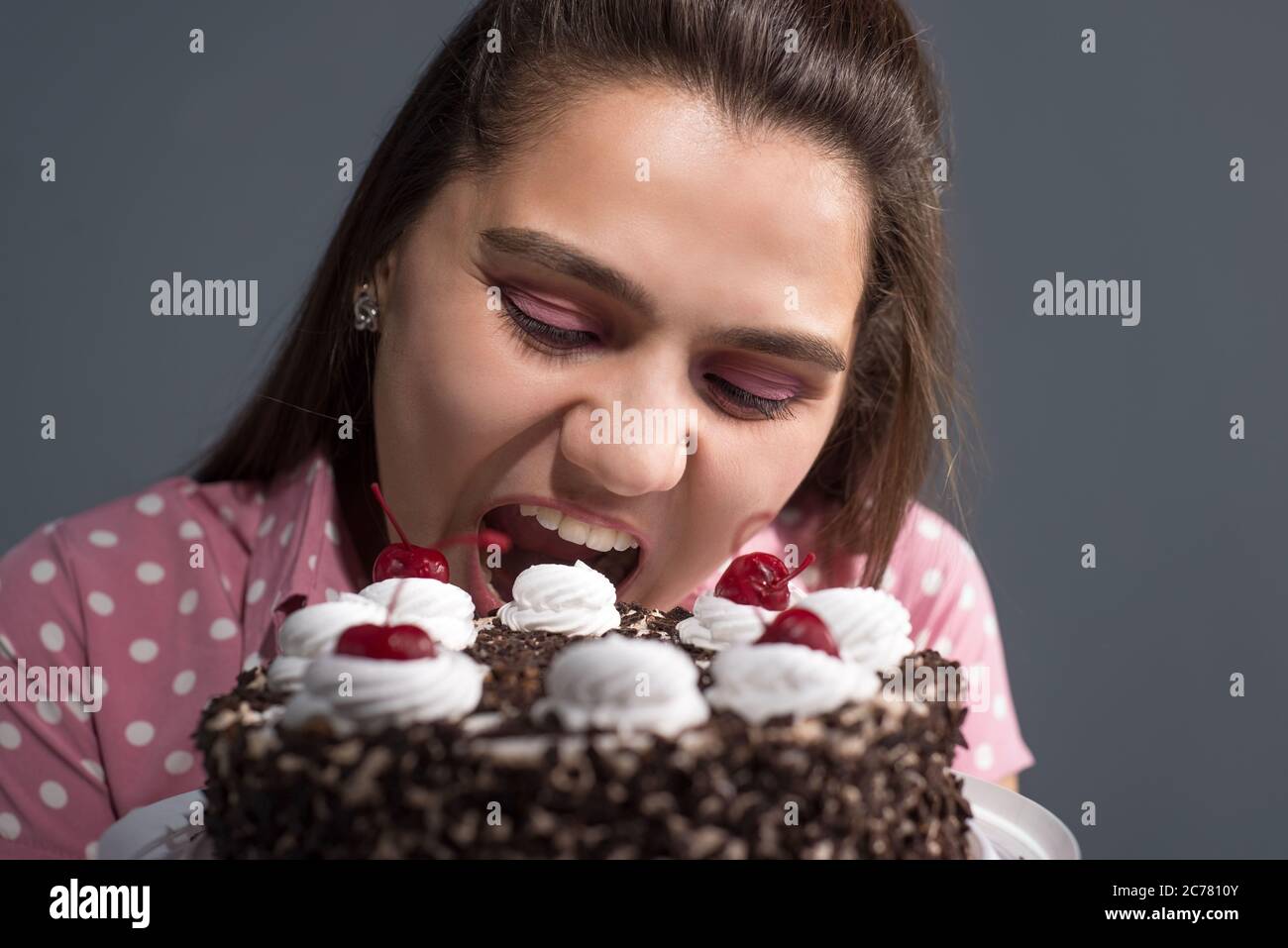 Portrait eines Mädchens, das einen Kuchen beißt. Studio Foto auf einem grauen Hintergrund Stockfoto