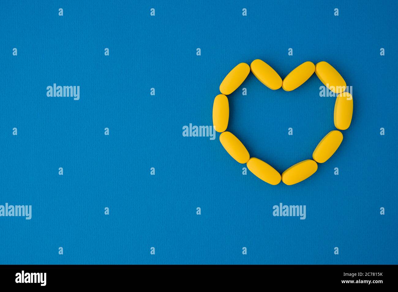 Gelbe Pillen Tabletten in Herzform auf blauer Oberfläche mit Kopieplatz Stockfoto