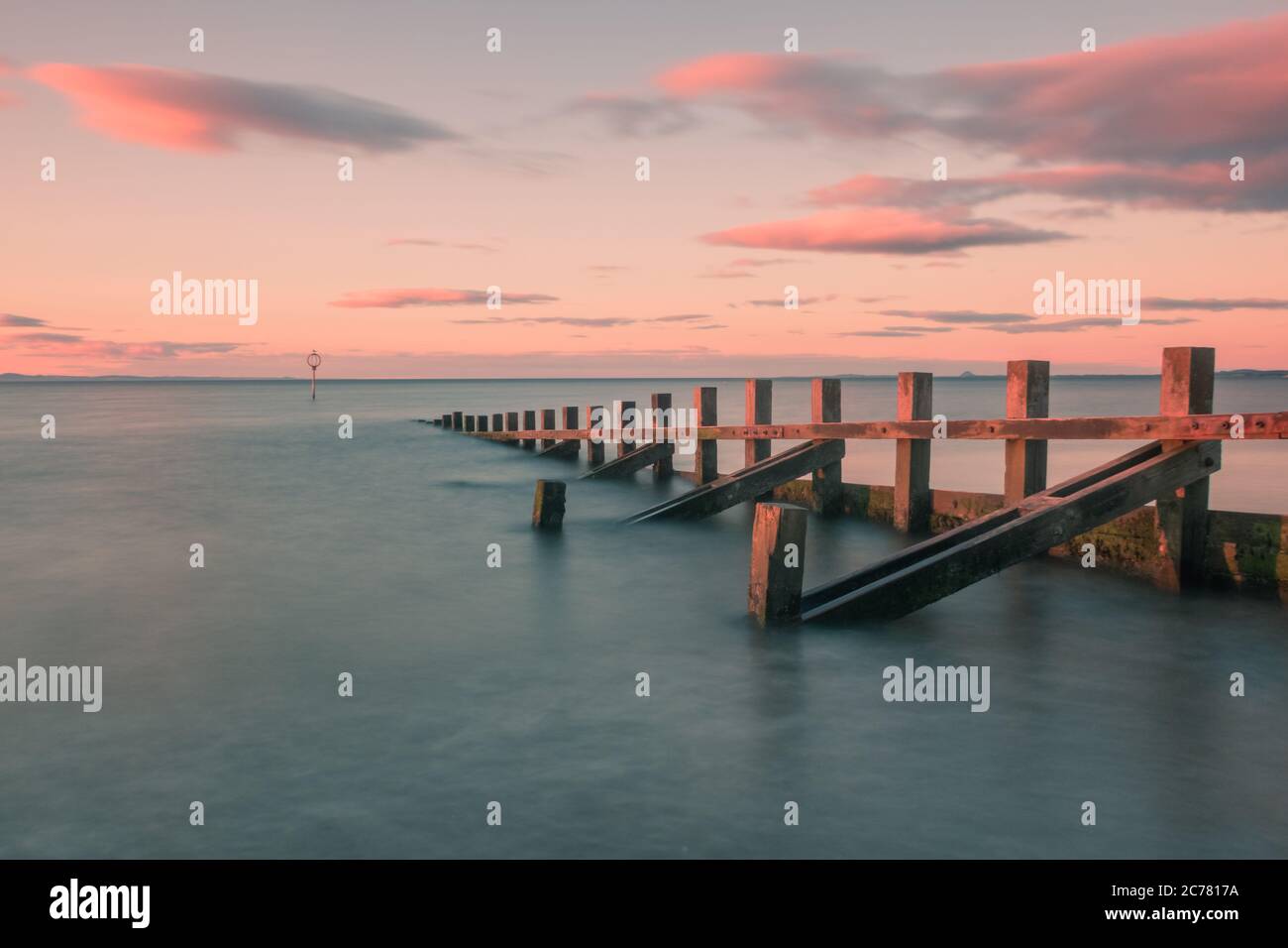 Eine hölzerne Groyne, die bei Sonnenuntergang ins Meer geht Stockfoto