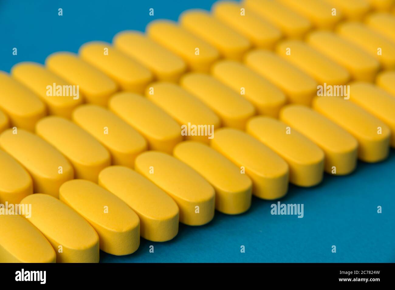 pharmakologie Industrie Konzept von vielen Reihen von gelben Pillen Tabletten von Vitamin-Medikamenten auf blauer Oberfläche Stockfoto