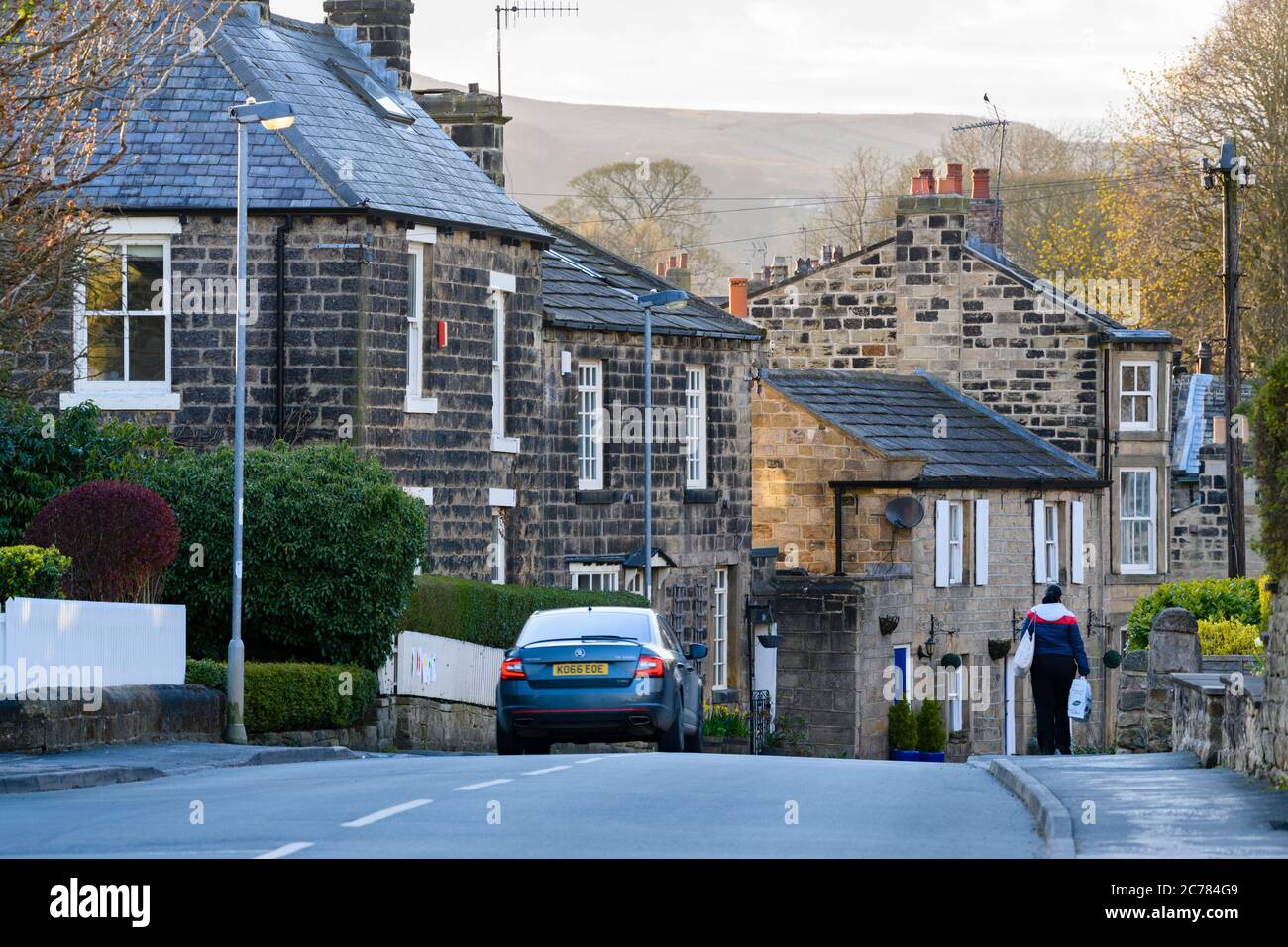 Hauptstraße in Menston Dorf (Frau, die an traditionellen Steinhäusern und Hütten vorbeiläuft) & landschaftlich reizvolle ländliche Moorlandschaft dahinter - West Yorkshire, England, Großbritannien. Stockfoto