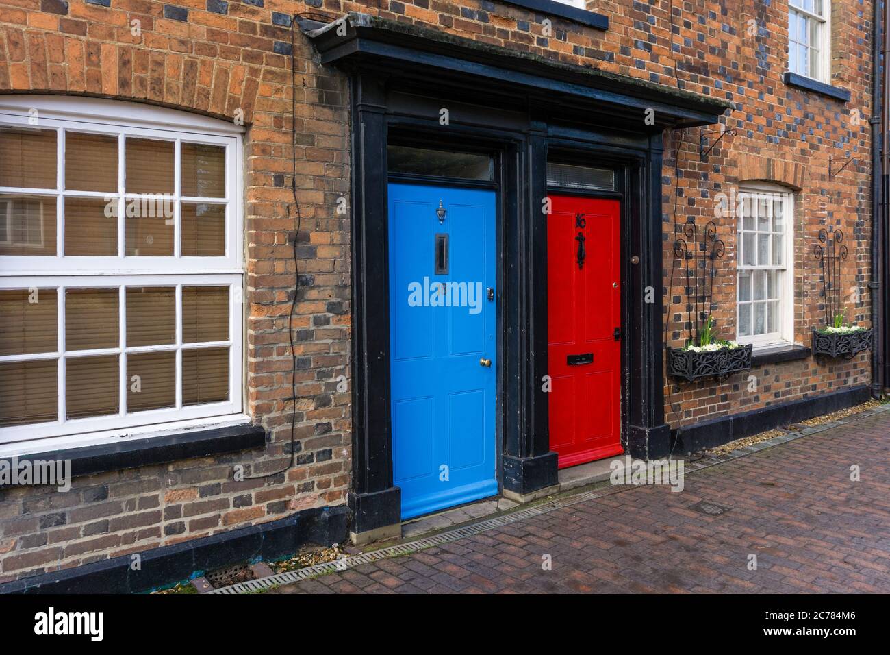 Angrenzende blaue und rote Türen in einer Terrasse von Häusern, Newport Pagnell, Großbritannien; Konzept für Konservative gegen Labour in der britischen Politik Stockfoto