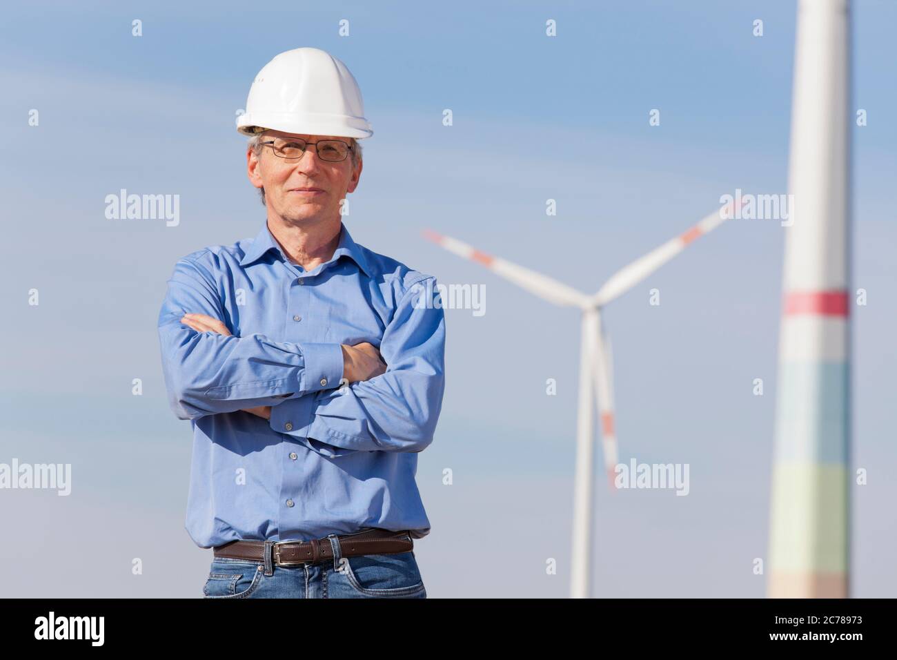 Lächelnder Ingenieur mit Hut vor einer Windmühle - konzentrieren Sie sich auf die Person Stockfoto